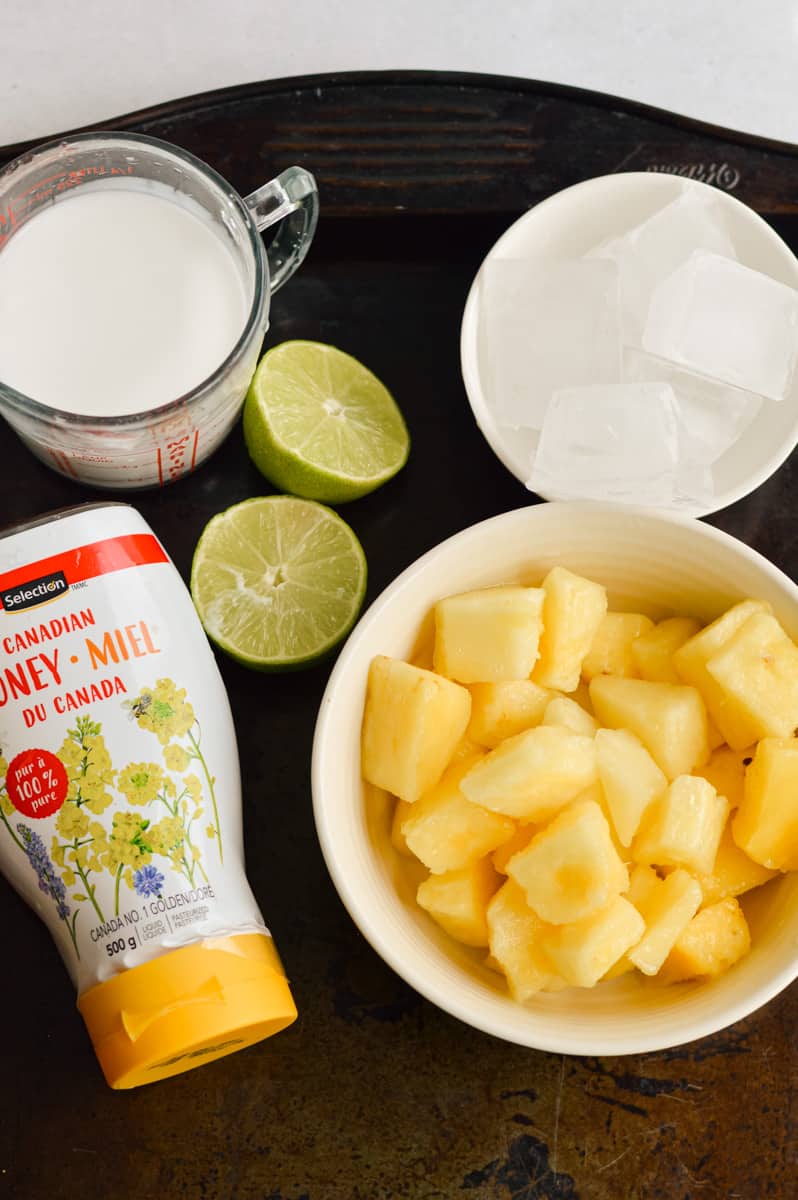Ingredients for pina colada mocktail including pineapple, lime, coconut milk and coconut shreds.