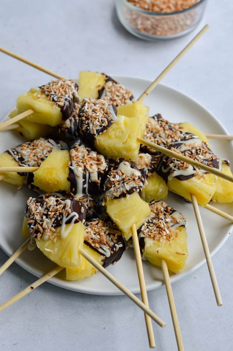 Plate of chocolate covered pineapples on skewers.