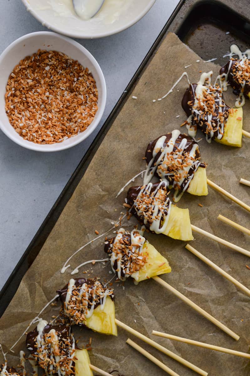 Sprinkling shredded coconut on chocolate covered pineapple.