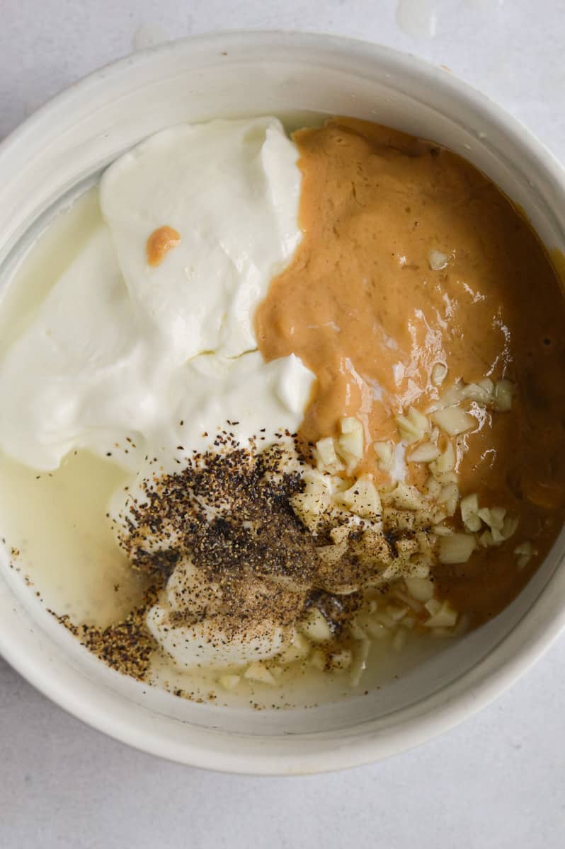 Addingg tahini, garlic, lemon juice, yogurt and spices to a bowl.