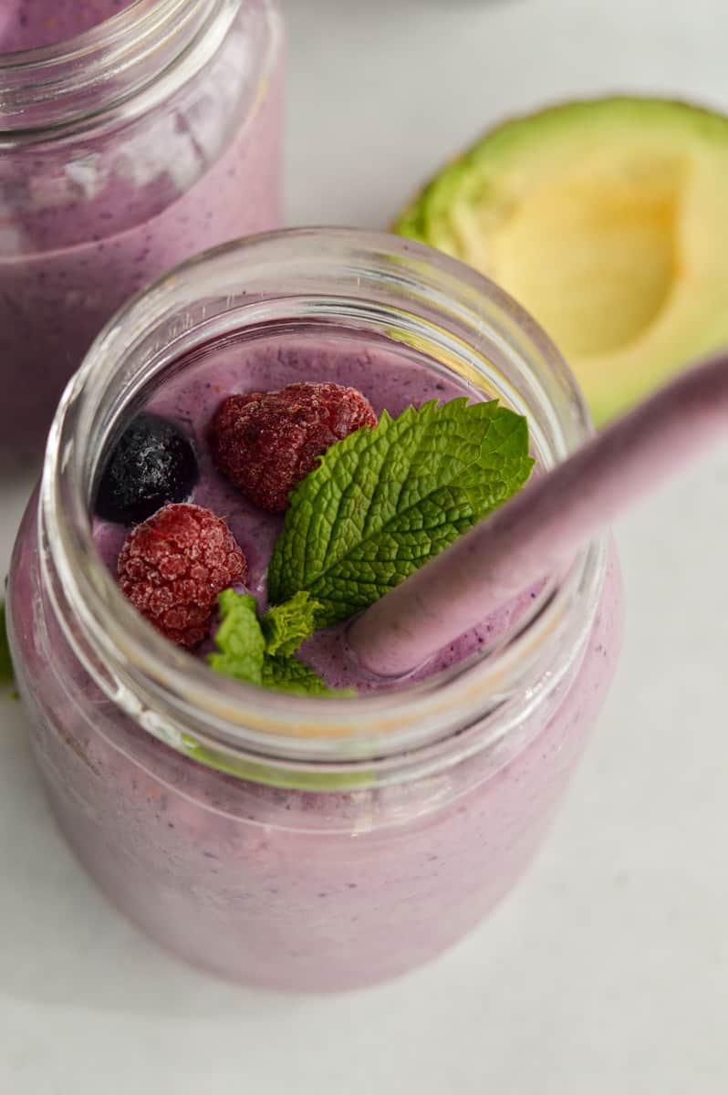 Berry high fiber smoothie with a straw, mint leaves and fresh berries.