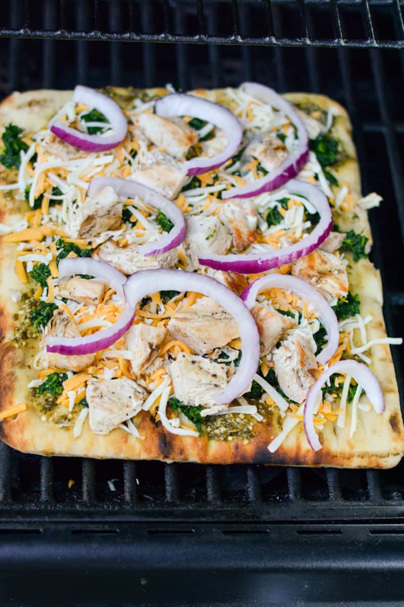 Adding chicken, spinach, pesto and red onion onto flatbread.