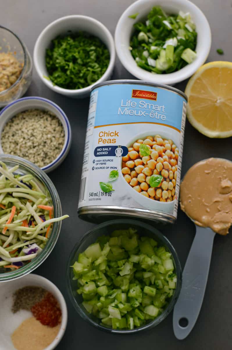 Ingredients including tahini, chickpeas, coleslaw, green onion, hemp seeds, lemon and red onion.