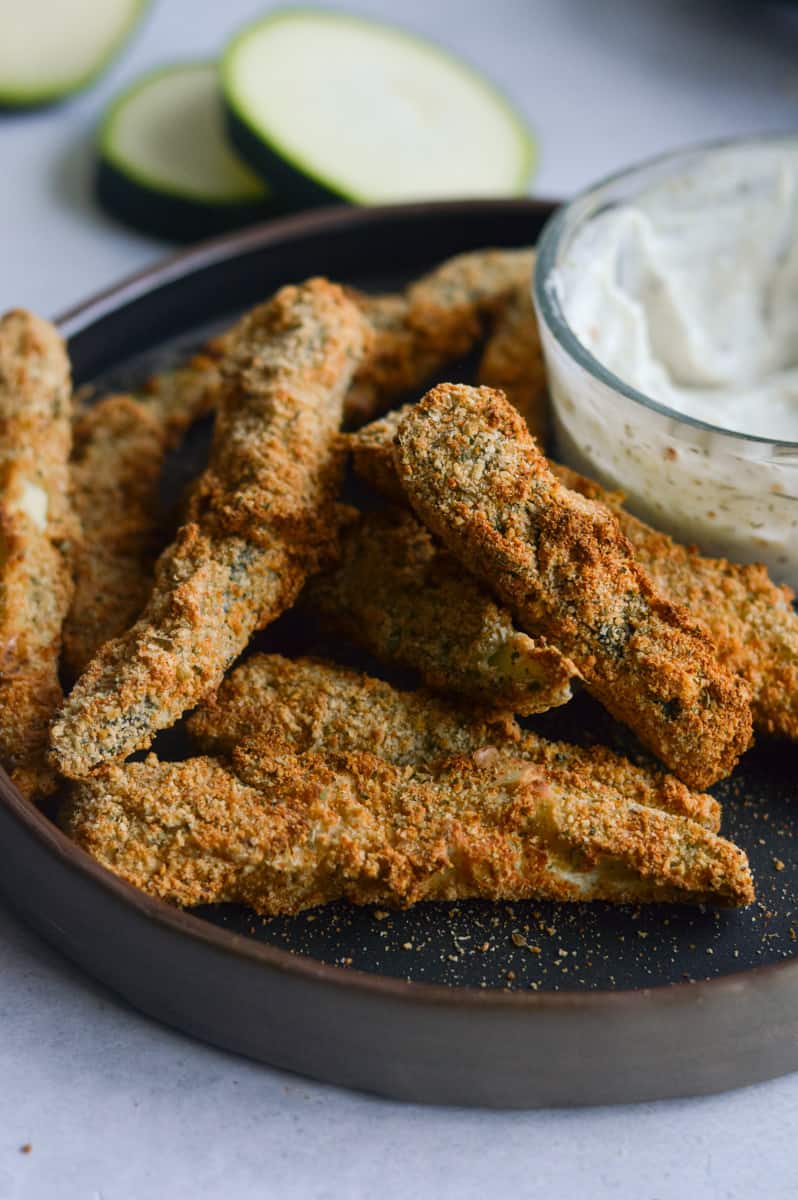Plate of air fryer vegan zucchini fries served with garlic yogurt dip.