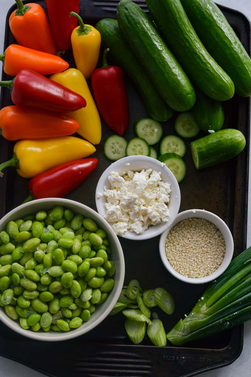 Ingredients including peppers, mini cucumbers, edamame, sesame seeds, and feta cheese.