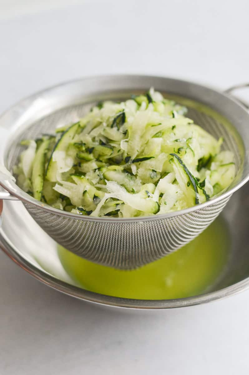 Straining liquid from shredded zucchini, using a colander.