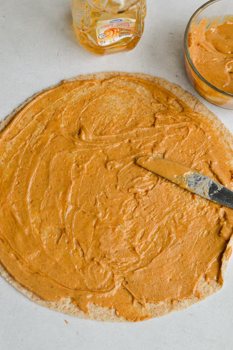 Spreading natural peanut butter on a whole wheat tortilla.
