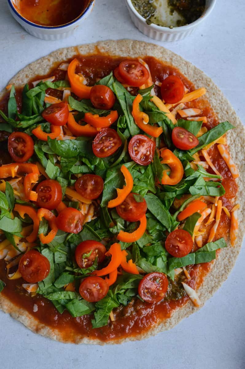Topping tortilla pizza with spinach, pepper and tomatoes.