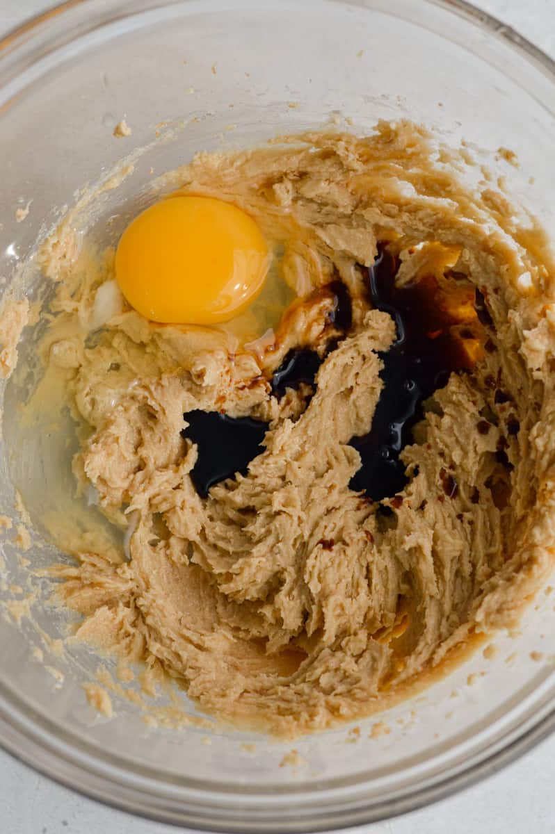 Adding an egg and vanilla extract to cookie dough.