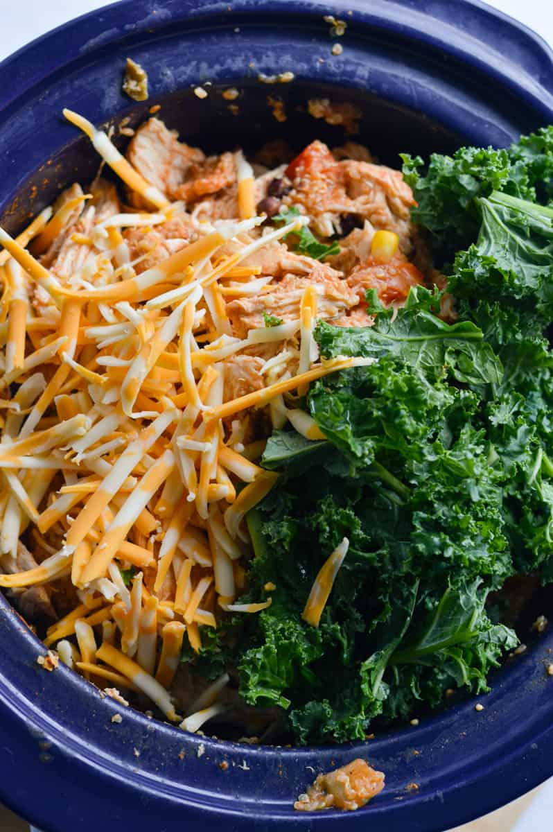 Adding cheese and kale into slow cooker.