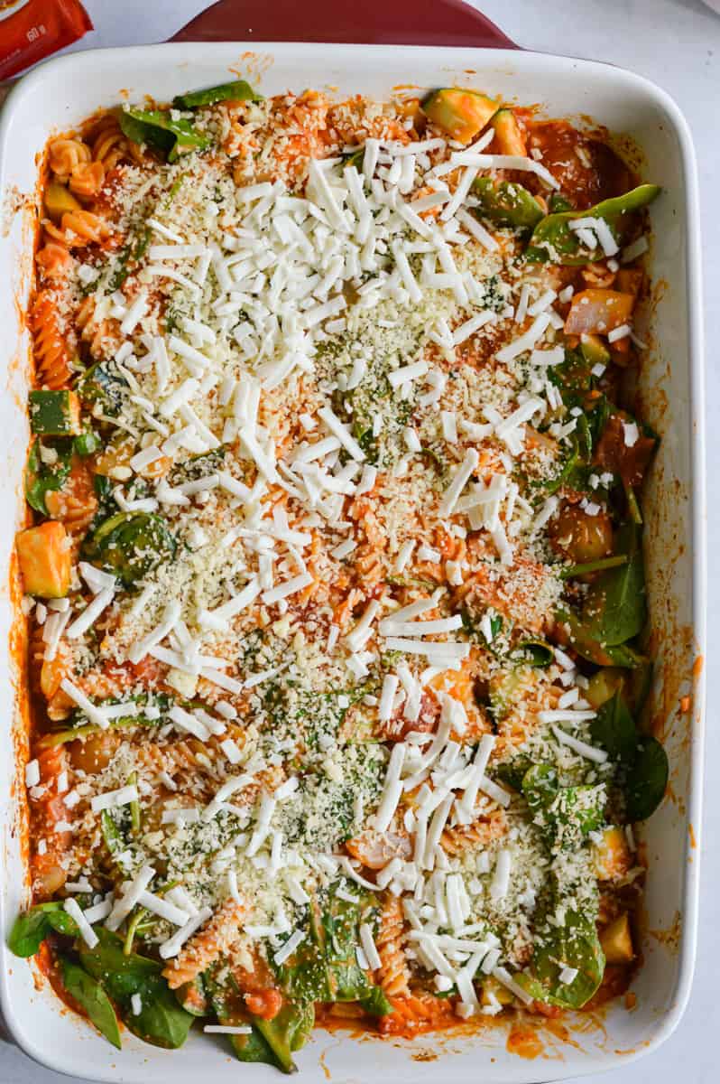 Adding spinach and vegan cheese to pasta bake.