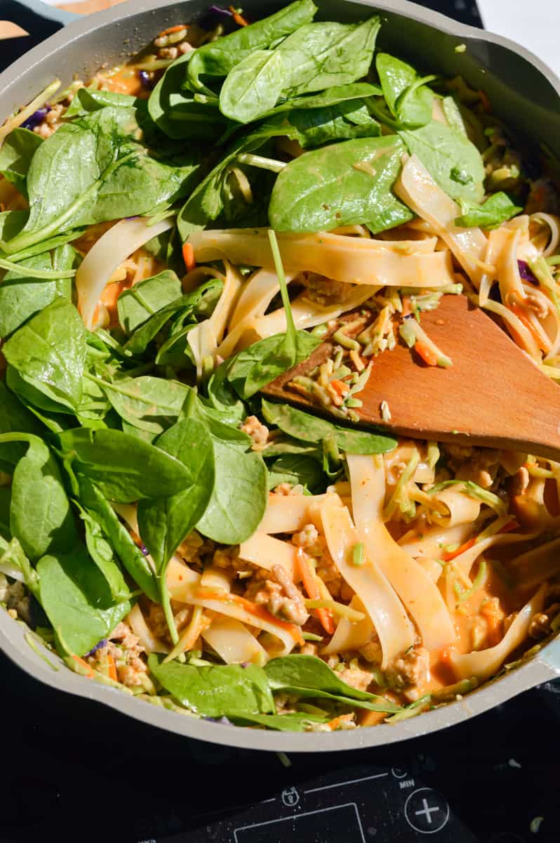 Adding a handful of spinach to peanut noodles.