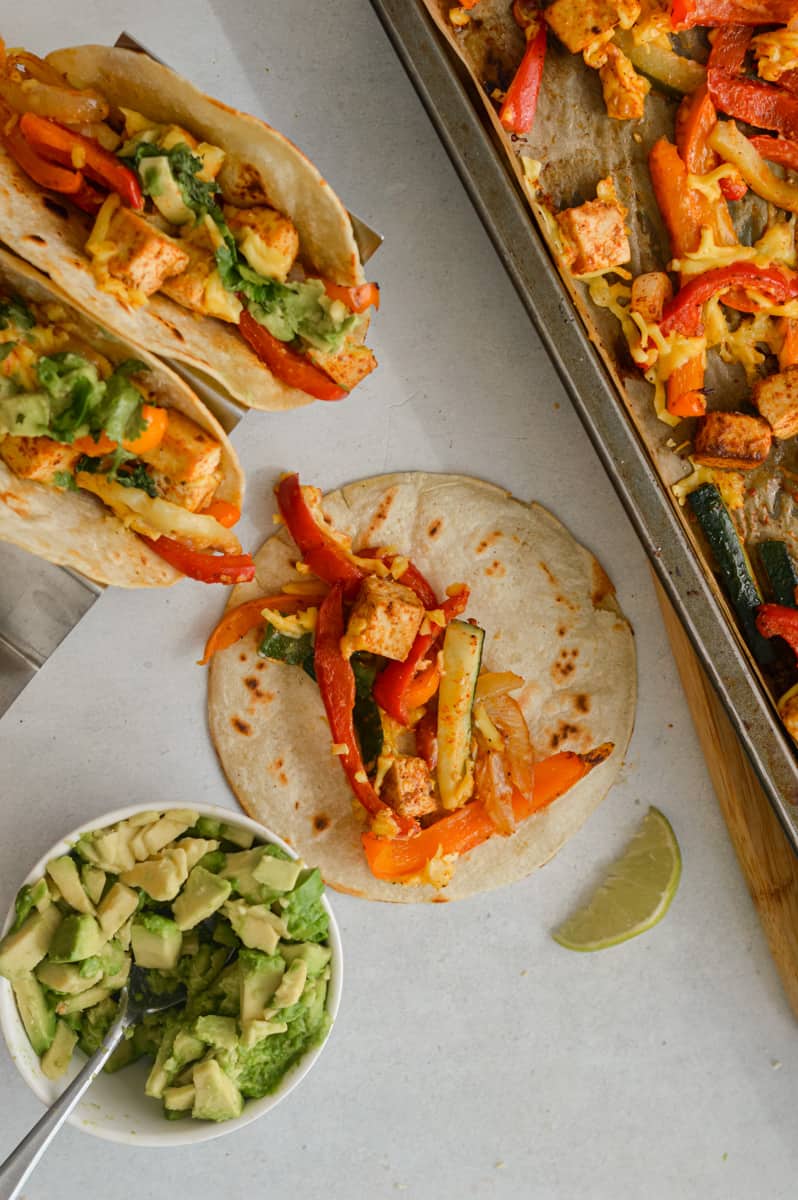 Birds eye of assembling tofu fajitas in a corn tortillas, topping with avocado.