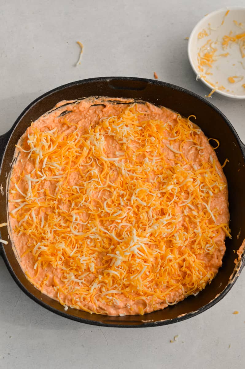 Sprinkling shredded cheese on buffalo chicken dip.