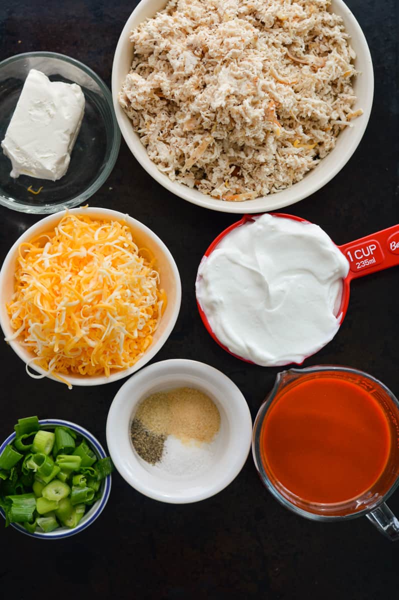 Ingredients includnig shredded chicken, cheese, Greek yogurt, seasoning, buffalo sauce, cream cheese and green onion.