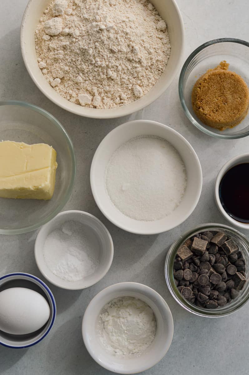 Portioned ingredients including brown sugar, white sugar, oat flour, egg, chocolate chips, salt, butter and vanilla extract.