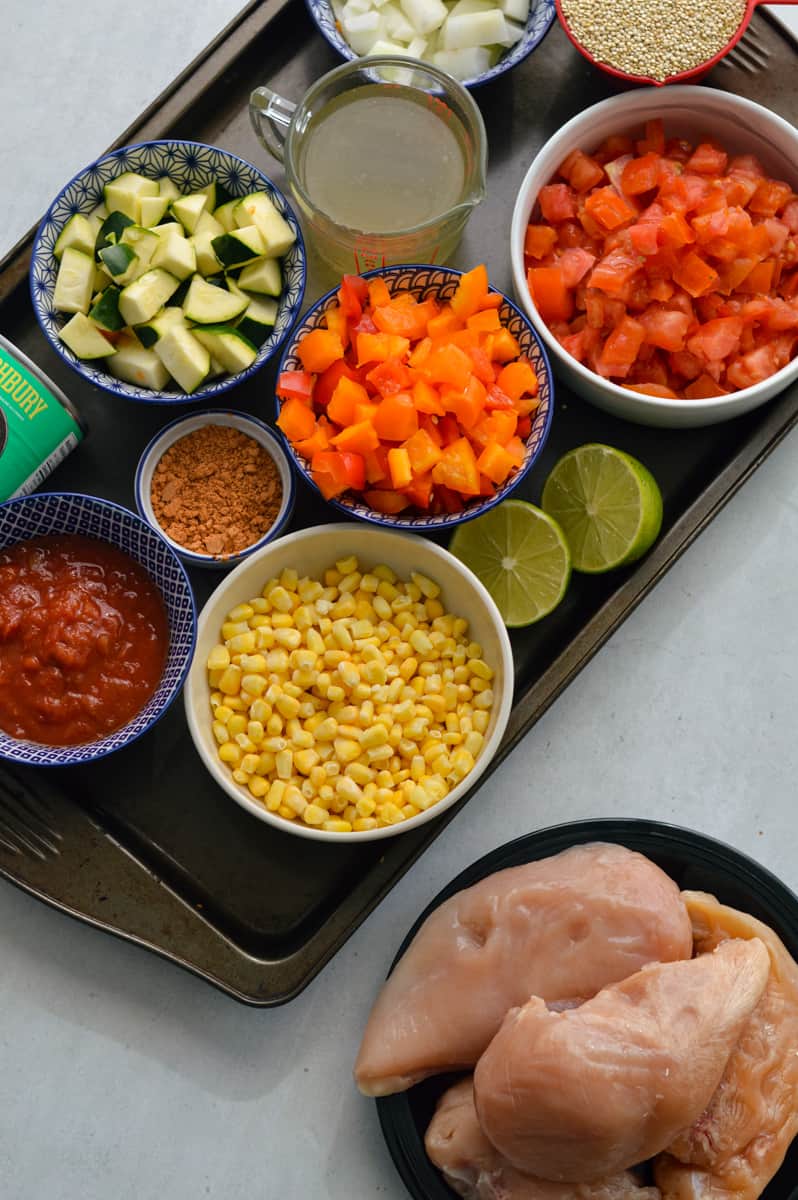 Ingredients including chicken breast, zucchini, diced tomatoes, corn, salsa, quinoa, bell peppers, lime, seasoning and cheese.