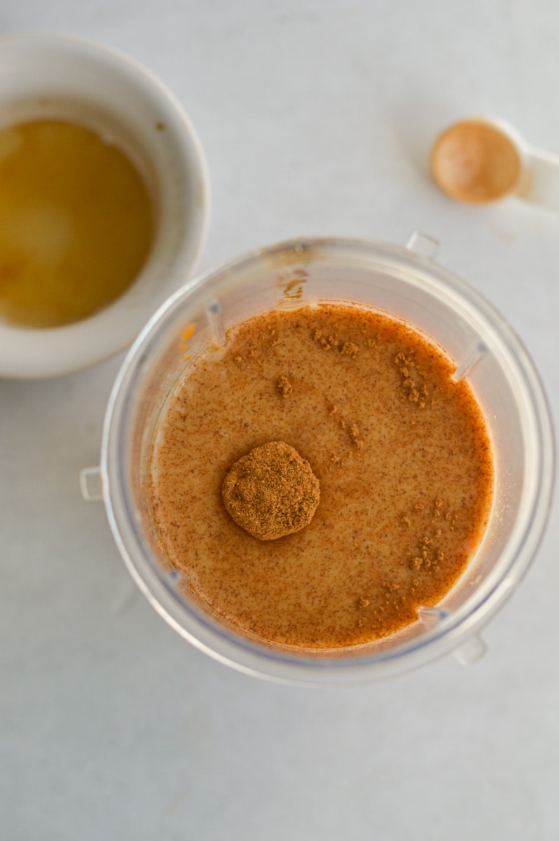 Adding milk, maple syrup, pumpkin puree, vanilla extract, and pumpkin pie spice to a blender.