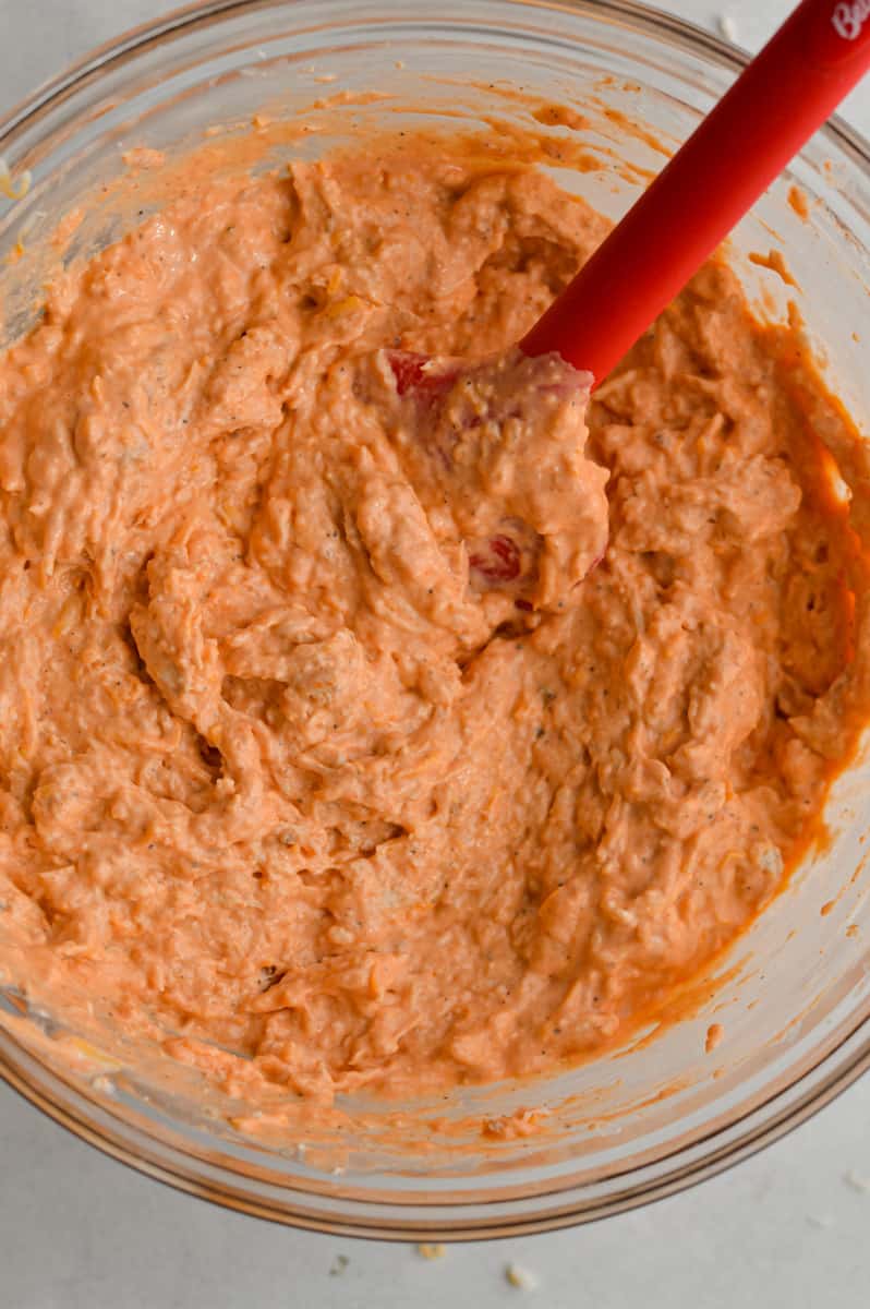 Mixing shredded chicken and cheddar cheese into dip.