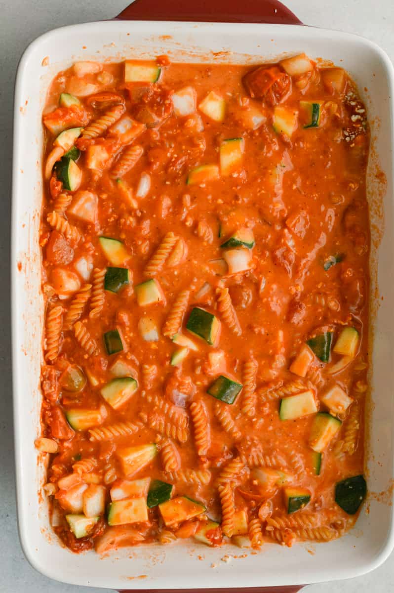 Adding coconut milk, marinara sauce, veggies and seasoning to a baking dish.