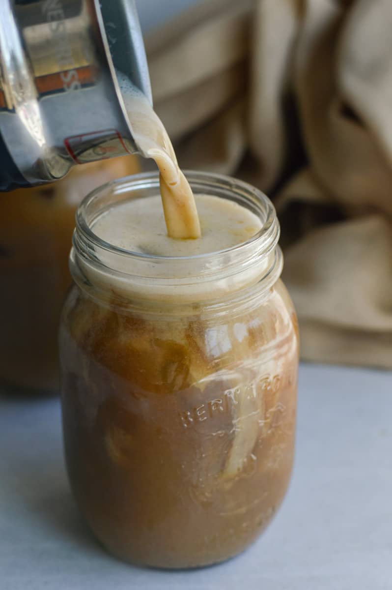 Pouring pumpkin cold foam onto cold brew.