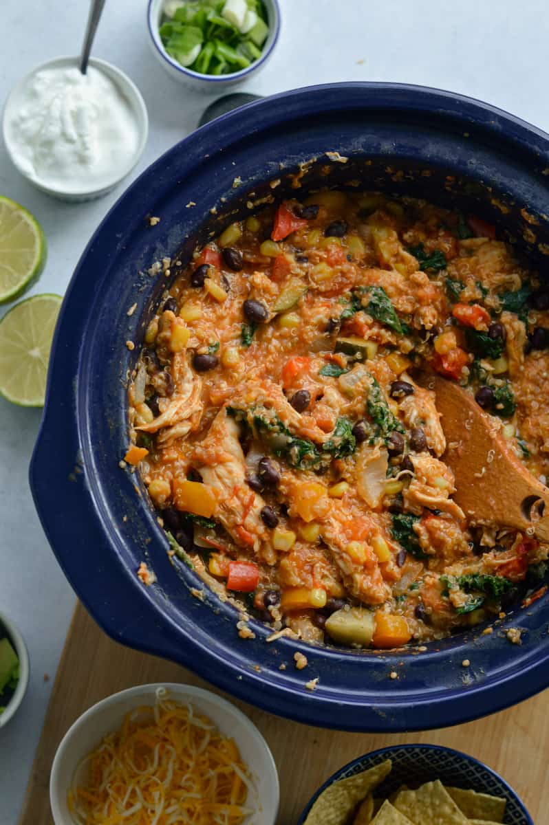 Slow cooker with southwest chicken bowls and toppings that include cheese, lime, yogurt and green onion. 