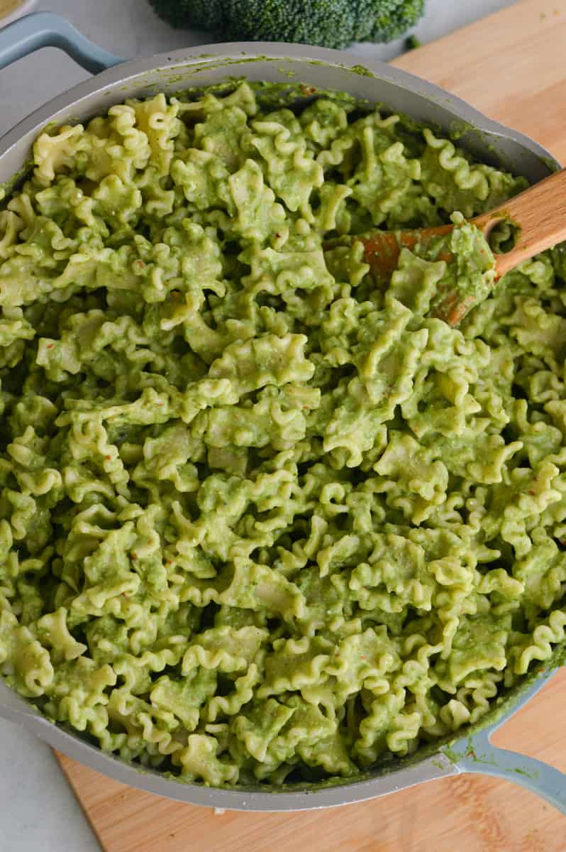 Stirring green pasta in a pan.