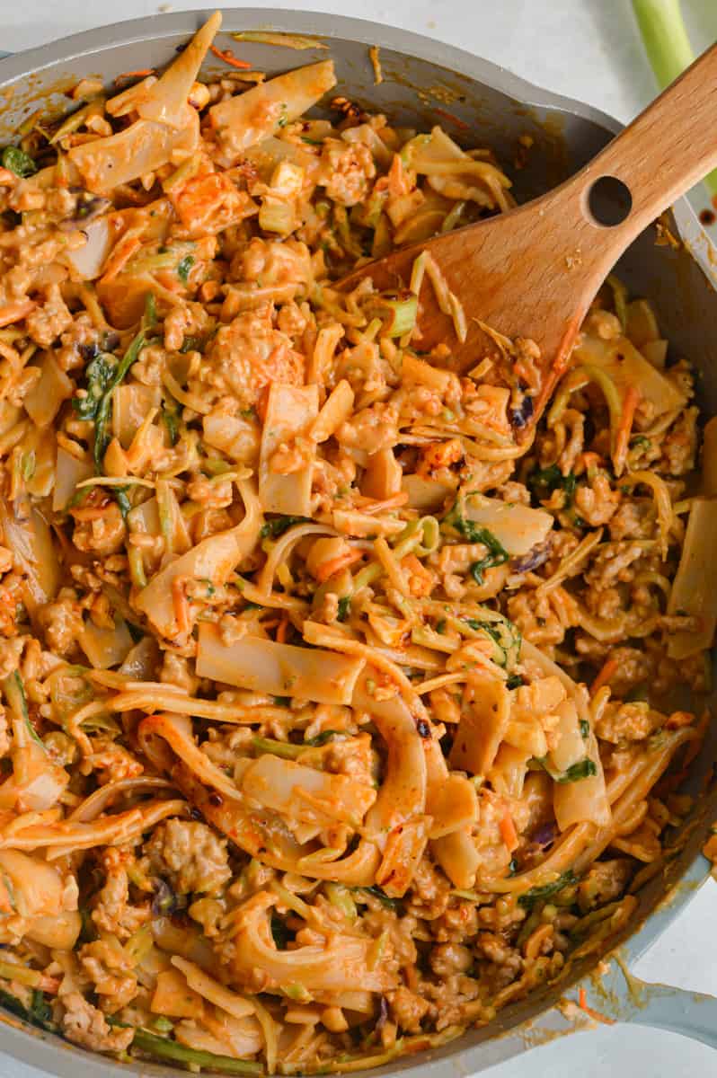 Stirring a pan of spicy peanut noodles with chicken.