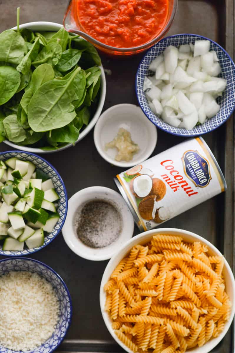 Ingredients including vegan cheese, coconut milk, chickpea pasta, onion, spinach, zucchini and spices.