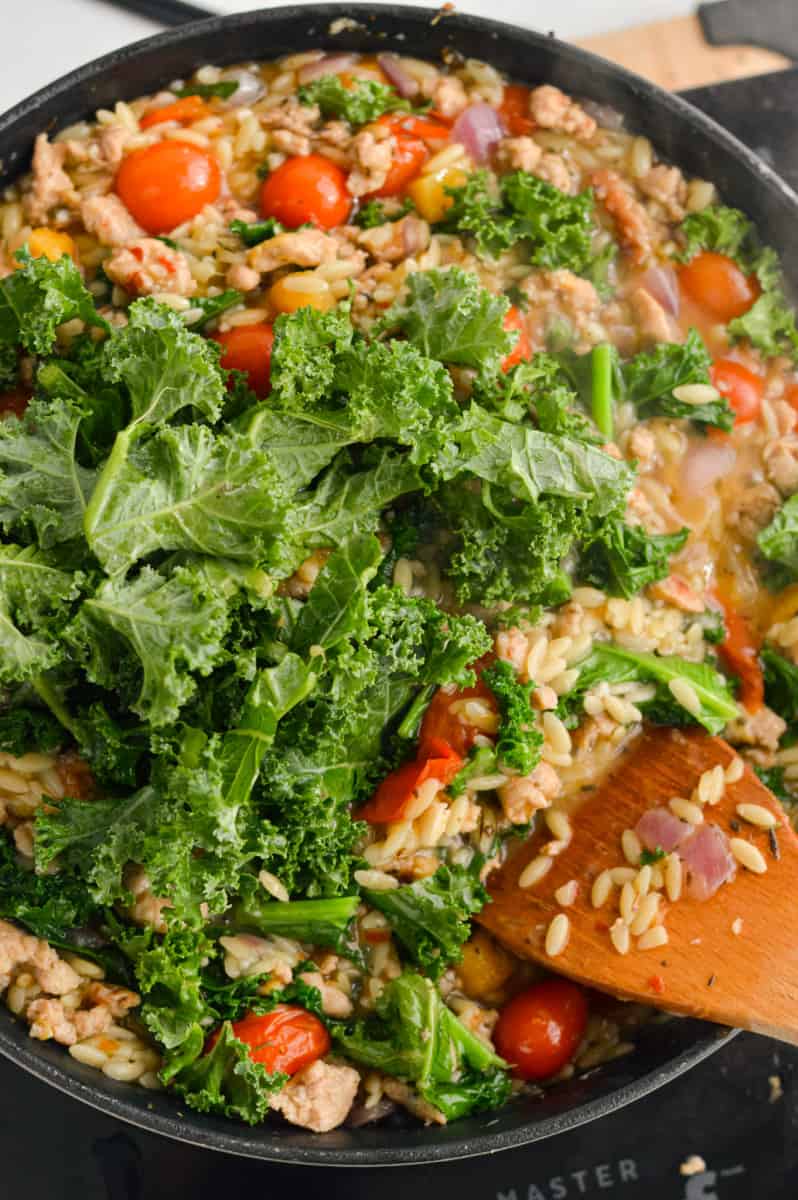 Adding kale into the orzo with sausage.