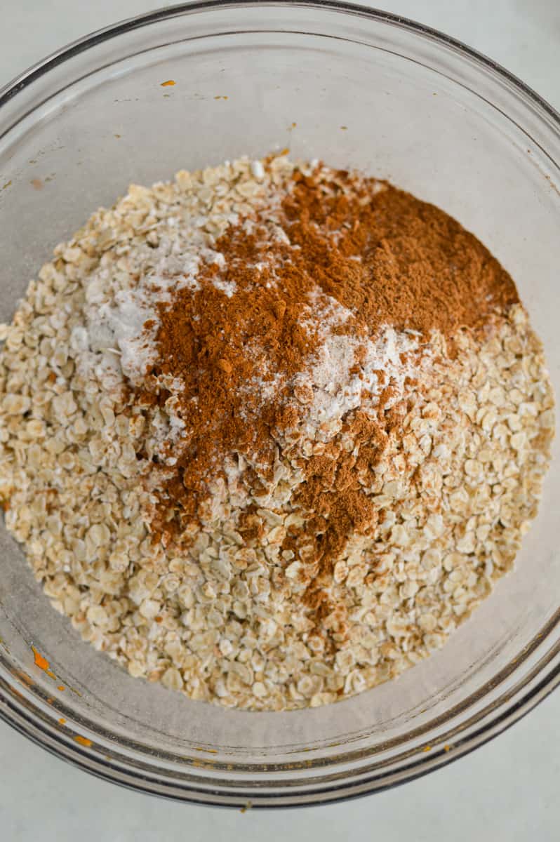 Adding oats, baking powder, cinnamon, pumpkin pie spice and salt to the bowl.