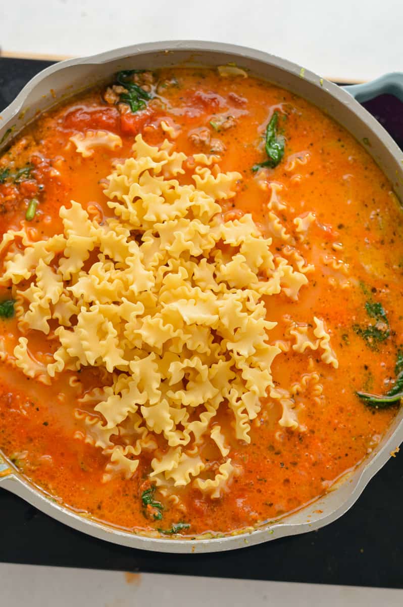 Adding milk, marinara sauce, broth and pasta to the pan.