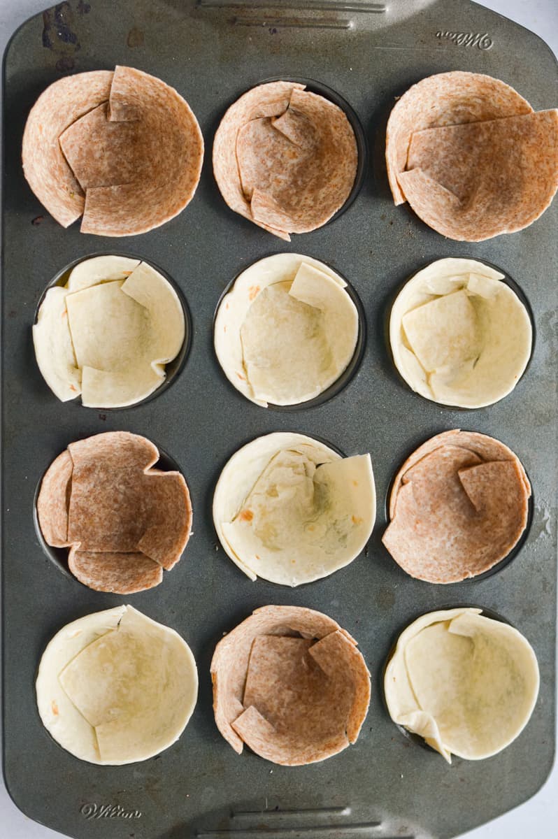 Folding tortillas into muffin tin to form pizza cup crust.