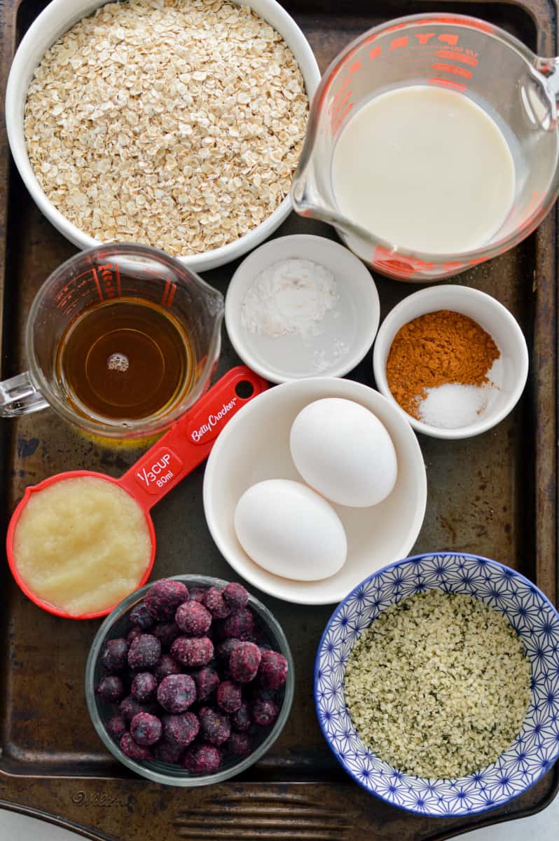 Ingredients including oats, eggs, milk, berries, applesauce, cinnamon, maple syrup, baking powder, hemp seeds and peanut butter.