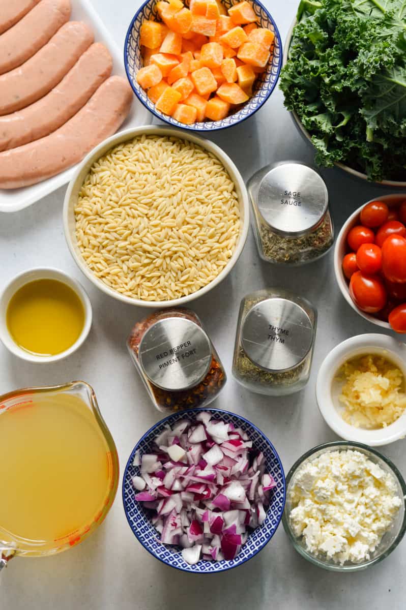Ingredients including olive oil, turkey sausage, kale, onion, feta, cherry tomatoes, spices, orzo, broth, garlic and feta.