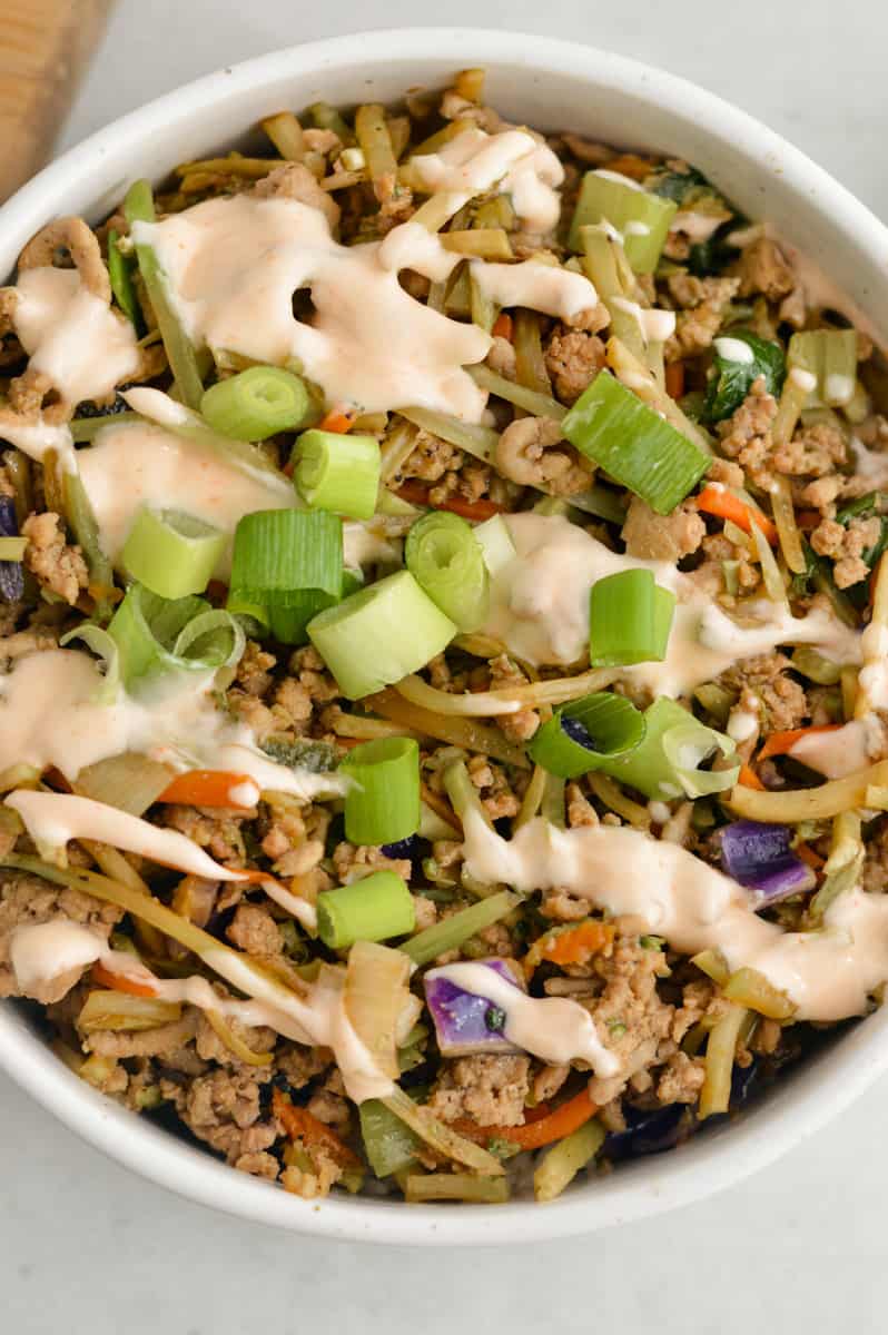 Close up of unstuffed egg roll bowls with sriracha mayo drizzled on top.