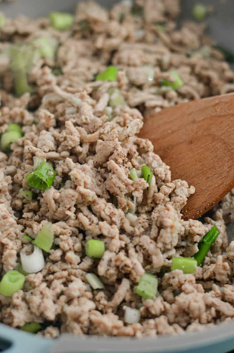 Cooking green onions and ground turkey in a pan.