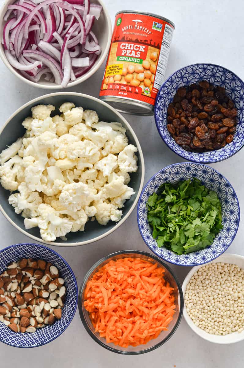 Ingredients including cauliflower, carrot, raisins, pearl couscous, red onion, chickpeas and cilantro.