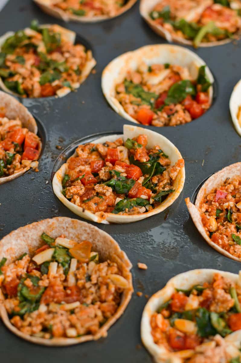 Filling muffin tin pizza cups with cooked turkey and veggie mixture.