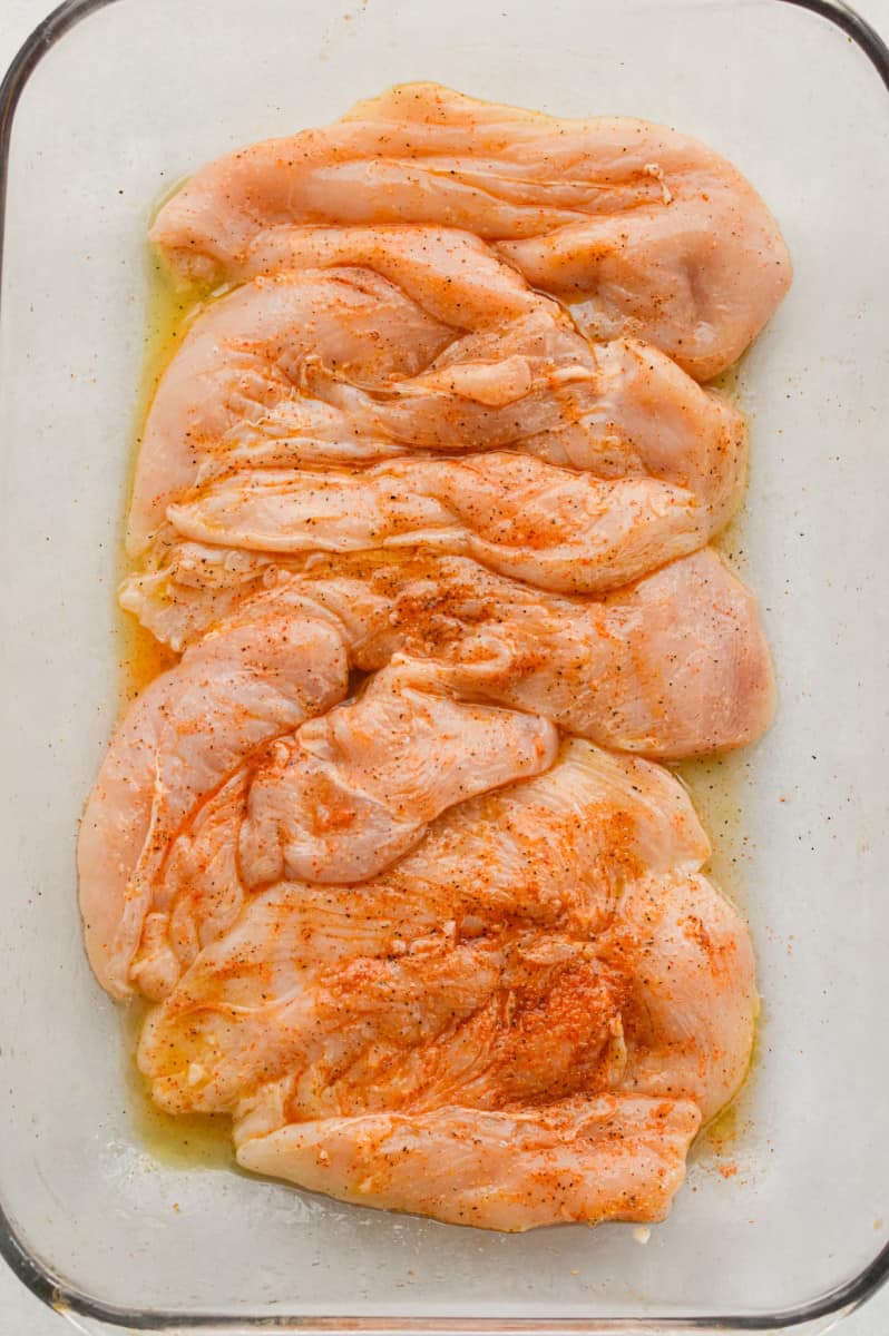 Coating chicken breast in olive oil and spices.
