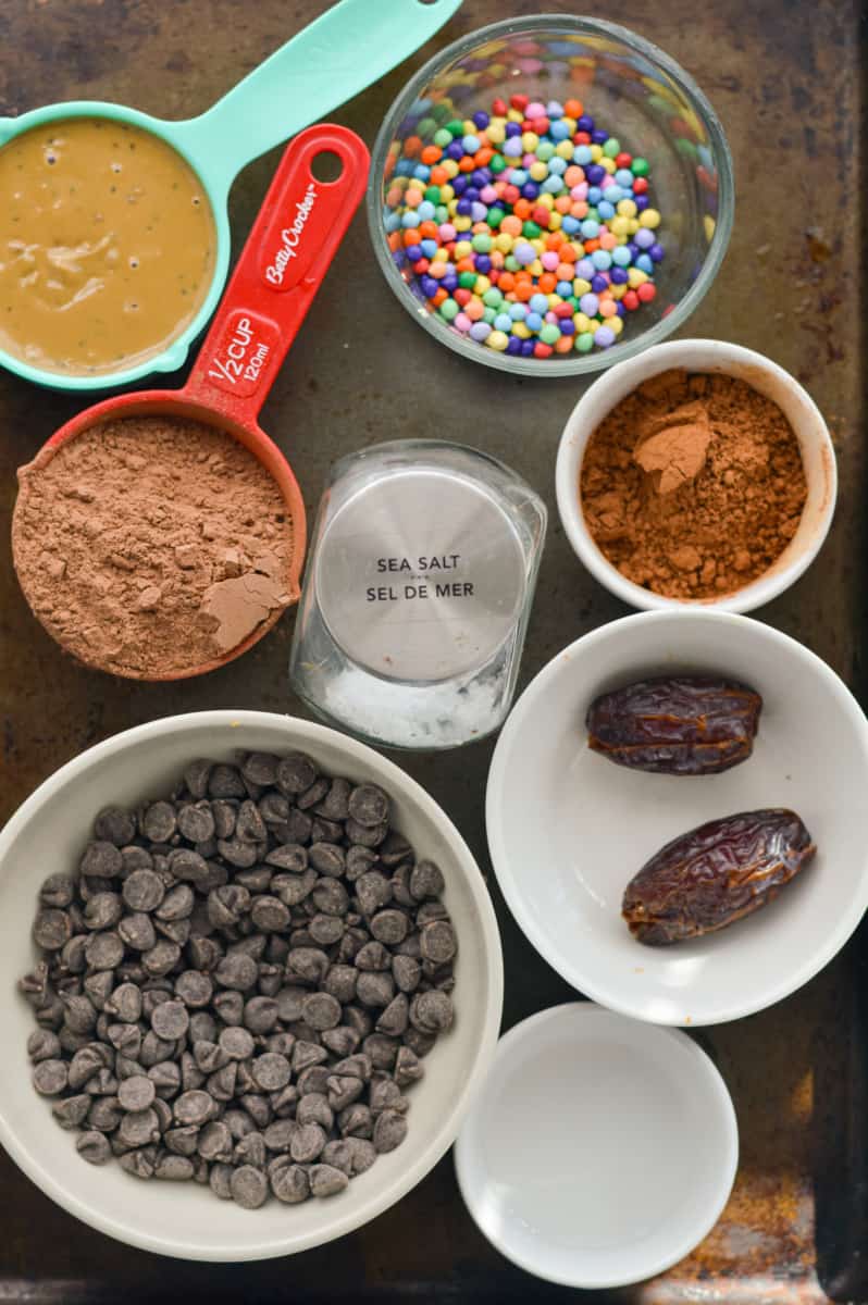 Ingredients including chocolate protein powder, dates, cocoa powder, chocolate chips, sprinkles and seed butter.