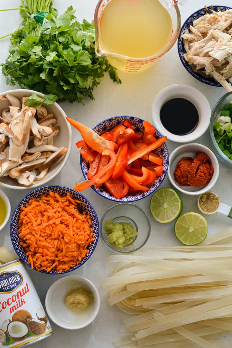Ingredients including seasoning, lime, veggies, chicken, chicken broth, lemongrass, rice noodles and fresh herbs.