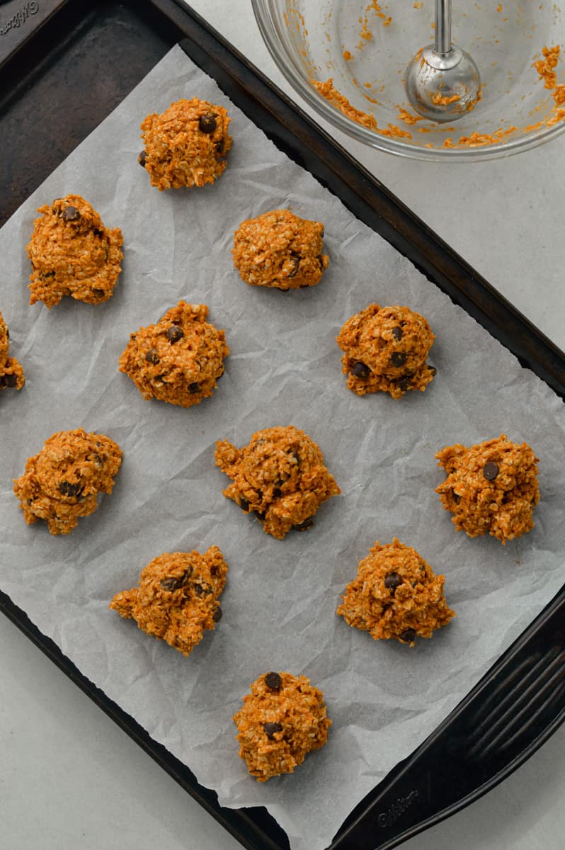 Scooping pumpkin oatmeal cookies onto a lined baking tray.