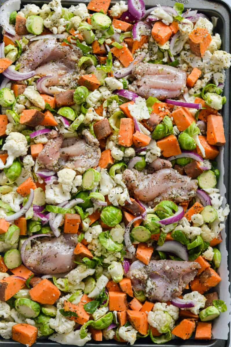 Spreading veggies and chicken thighs onto a sheet pan.