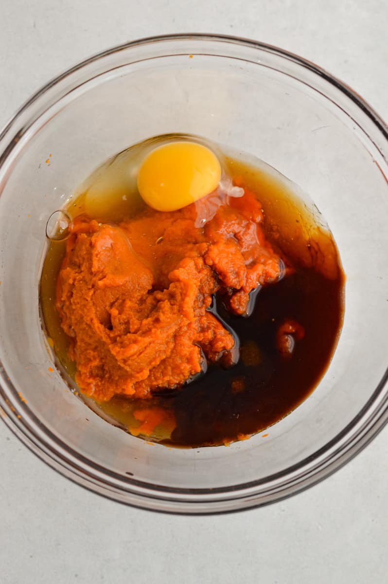 Adding egg, maple syrup, vanilla and pumpkin puree to a bowl.