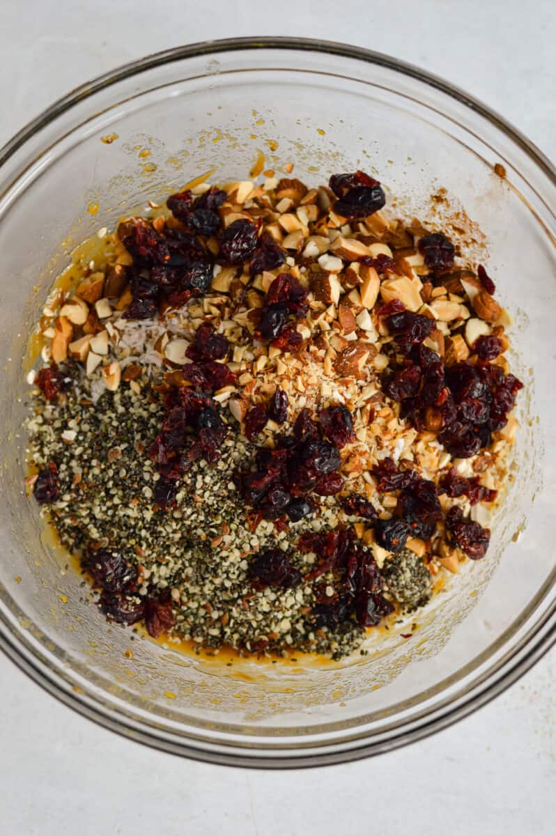 Adding oats, chopped almonds, shredded coconut, hemp seeds, cinnamon, protein powder and dried cranberries.