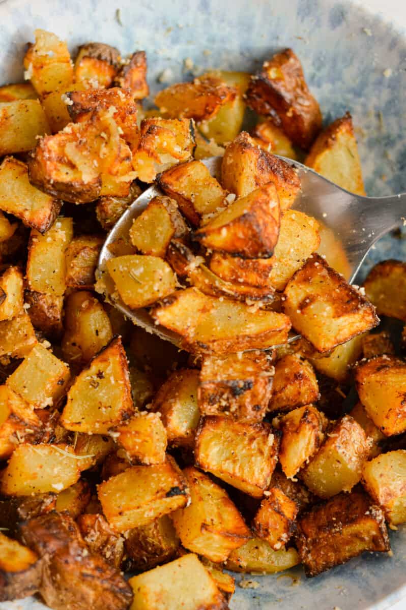 Close up of crispy air fryer diced potatoes in a bowl with a spoon.