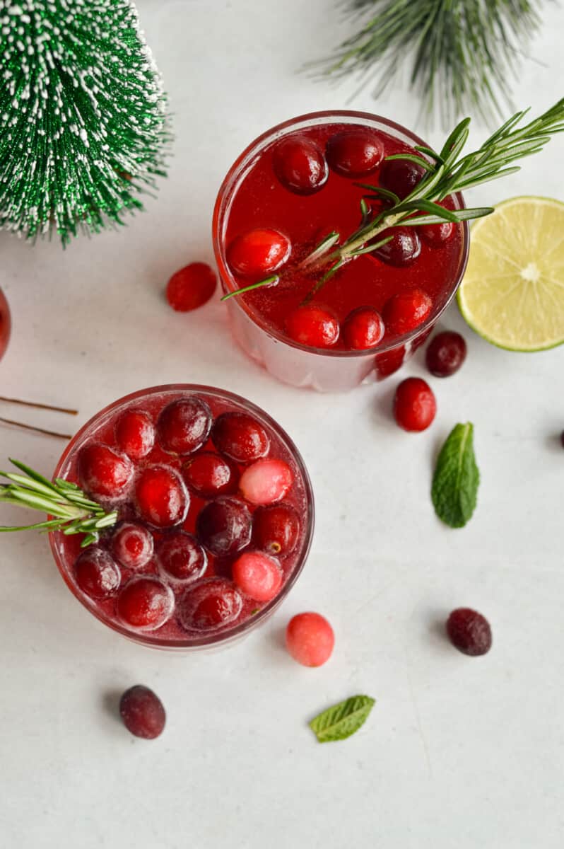 Birds eye of two cranberry ginger beer mocktails topped with frozen cranberries and mint leaves.