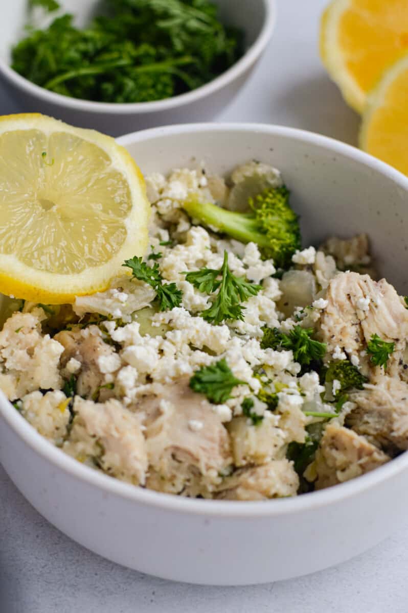Bowl of lemon garlic chiekn and rice, topped with parsley, feta and a lemon slice.