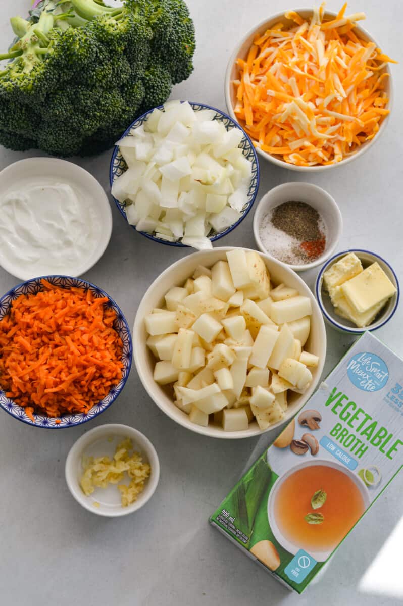 Ingredients including broccoli, carrot, onions, garlic, butter, Greek yogurt, potatoes, cheddar, broth and spices.